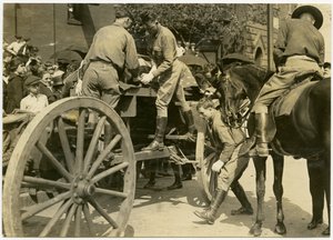 Horisontalt sepia -fotografi, hvor uniformerede mænd læser en genstand, der er draperet i det amerikanske flag, muligvis en kiste, ud af en åben vogn. En skare mennesker ser på fra fortovet